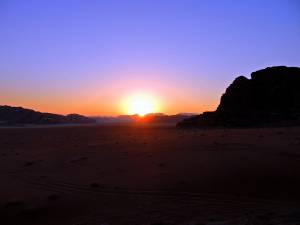 Jordanien | Sonnenuntergang im Wadi Rum. Umgeben von einigen Bergen geht die Sonne am Horizont bei blau, rosa, gelb gefärbtem Himmel unter
