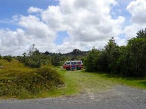 Neuseeland | Nordinsel, Unser Stellplatz auf der Uretiti Campesite im hohen Norden. Unser Hippie Camper steht umgeben von grünen Büschen auf einem idyllischen Plätzchen mit den beiden Campingstühlen im Vordergrund