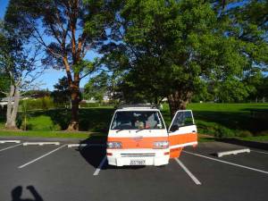 Neuseeland | Nordinsel, Camping direkt bei der iSITE in Whangarei im hohen Norden. Unser Hippie Camper steht auf dem Parkplatz mit grüner Wiese im Hintergrund unter Bäumen bei blauem Himmel und Sonnenschein