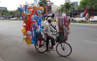 Vietnam | Süden, Straßenverkäufer von Ho Chi Minh City. Ein Mann auf seinem Fahrrad mit Luftballons und Kinderspielzeug zum Verkauf. Reise-Highlights & Tipps findest Du in unserem Reisebericht