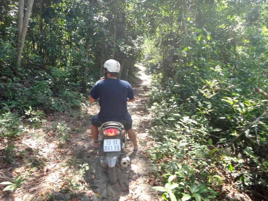 Vietnam | Süden, Moped Tour durch den Urwald. henning sitzt auf dem Moped auf einem schmalen Weg fahrend, der mitten in den Urwald führt