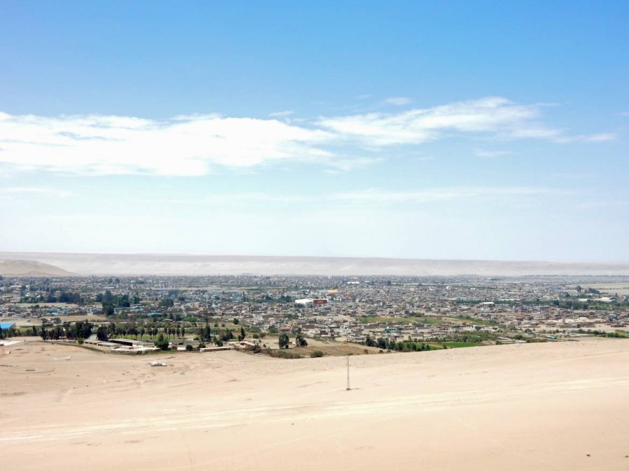 Chile | Peru, Ankunft in Tacna beim Weg über die Grenze Grenze von Arica nach Tacna. Die Stadt im Hintergrund, Wüste im Vordergrund bei blauem Himmel