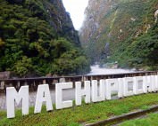Peru | Machu Picchu, Inka-Stadt und Weltwunder. Blick auf die weißen Buchstaben Machu Picchu vor dem Fluss und grünen Bergen im Urubamba Tal