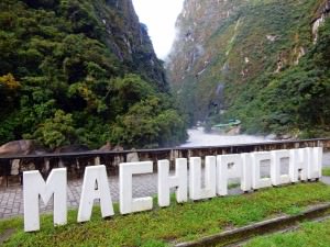 Peru | Machu Picchu, Inka-Stadt und Weltwunder. Blick auf die weißen Buchstaben Machu Picchu vor dem Fluss und grünen Bergen im Urubamba Tal