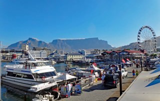 Südafrika | Kapstadt, Panorama in der V&A Waterfront mit dem Tafelberg im Hintergrund. Boote, Restaurants, Shops, Touristen bei blauem Himmel