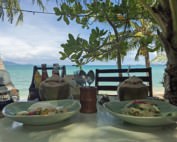 Thailand | Koh Samui, Mittagessen direkt am Strand mit traumhaftem Ausblick, hier am Maenam Beach. Zwei Teller mit Reis und Curry, zwei Kokosnüsse auf gedecktem Tisch, im Hintergrund das türkisfarbene Meer