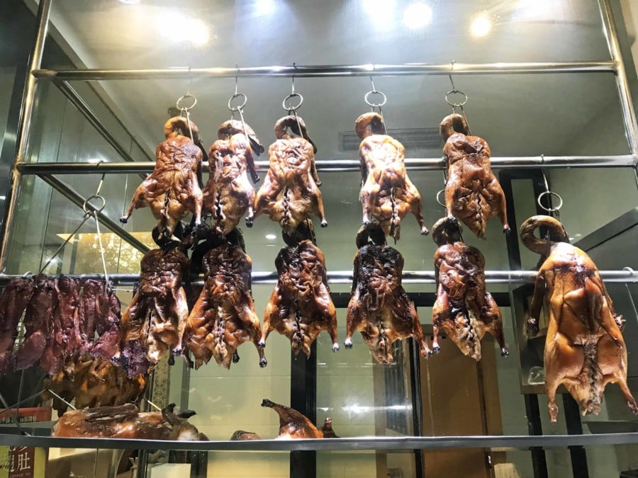 Peking Ente als Street Food Gericht. Am Haken hängende ganze Enten in einem Fenster